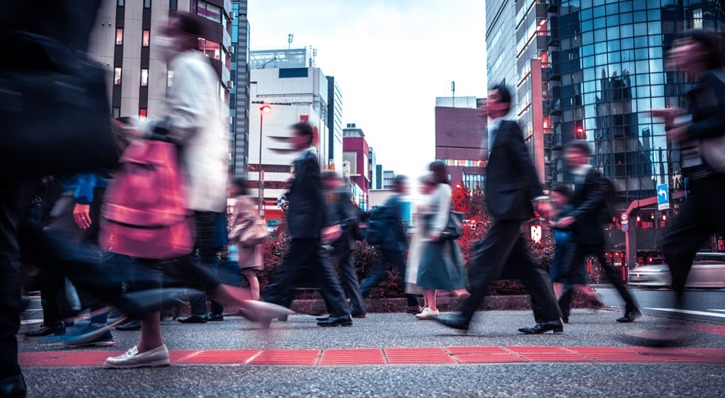 Many people hustling and bustling in a downtown area. There are tall buildings and skyscrapers in the background.