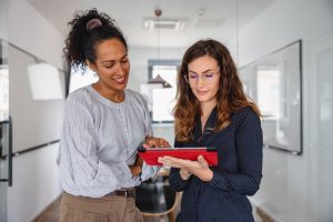 Two Female Colleagues Talking In The Office And Using Digital Tablet