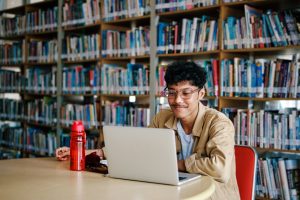 Young Stylish Adult Man Studying at Library with Laptop