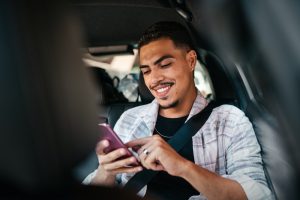Young man smiling while using his smartphone in the car