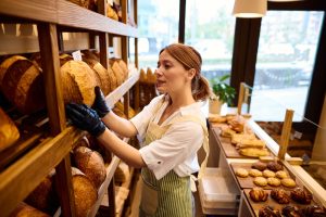 Baker arranging fresh bread loaves on shelves in bakery shop